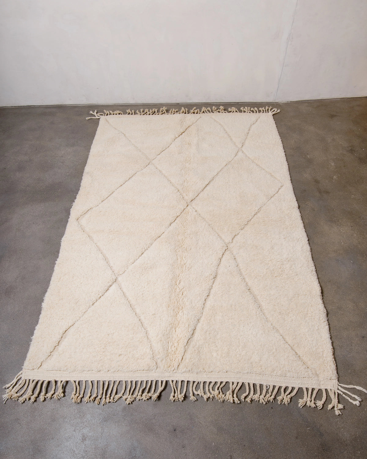 Berberlin Beniourain Rug made of natural cream wool with a woven diamond design, photographed on a concrete floor.